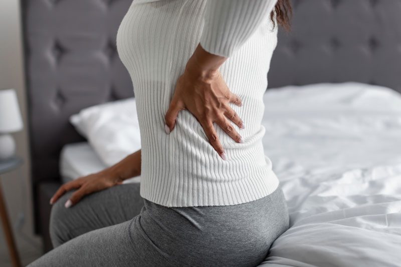 woman with side back pain sitting on bed at home